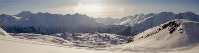 A wide panoramic view of a snow-covered mountain range in Alaska at sunrise or sunset.